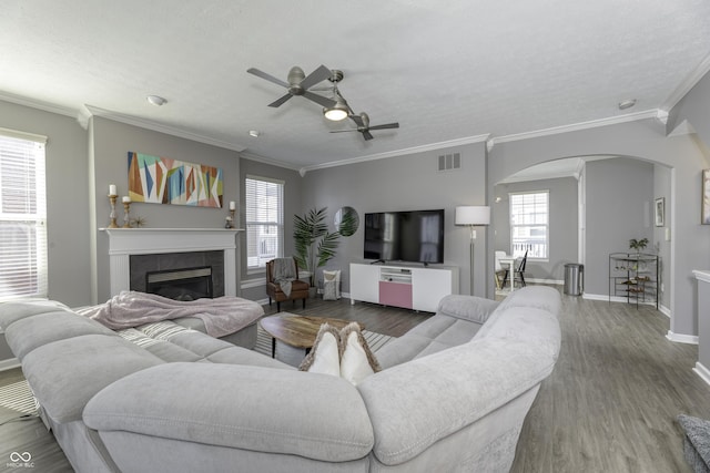 living area featuring arched walkways, a textured ceiling, a tile fireplace, wood finished floors, and baseboards