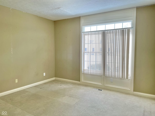 unfurnished room with a textured ceiling, carpet floors, baseboards, and a healthy amount of sunlight