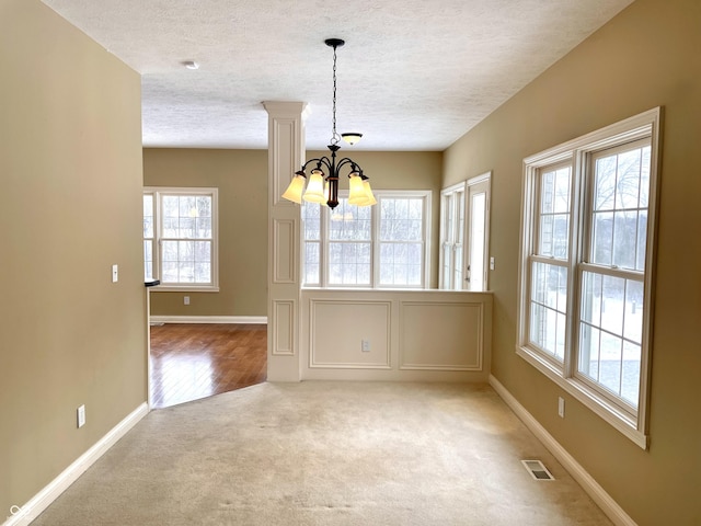 unfurnished dining area with visible vents, baseboards, an inviting chandelier, carpet, and a textured ceiling