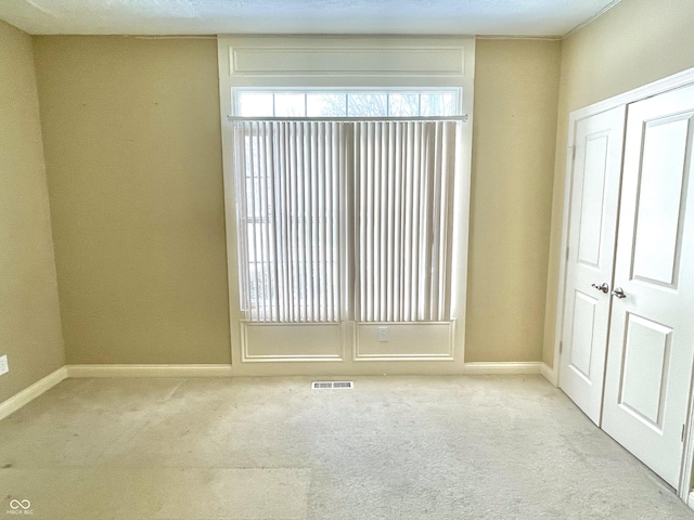 empty room featuring baseboards, visible vents, and light colored carpet