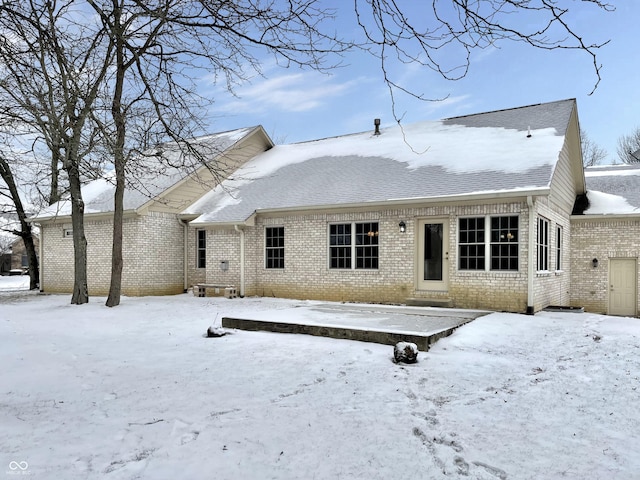 snow covered rear of property featuring entry steps, roof with shingles, and brick siding