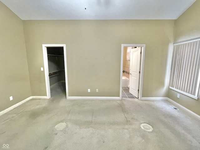 unfurnished bedroom with carpet floors, a walk in closet, visible vents, and baseboards