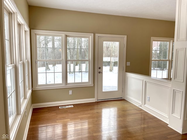 doorway featuring hardwood / wood-style flooring, wainscoting, visible vents, and a decorative wall