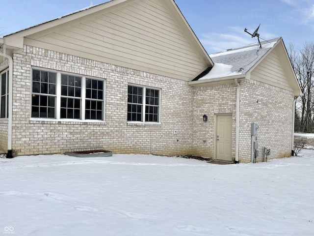 snow covered house featuring brick siding