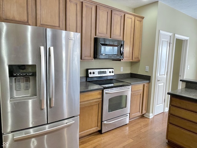 kitchen featuring stainless steel appliances, dark countertops, brown cabinetry, and light wood-style floors