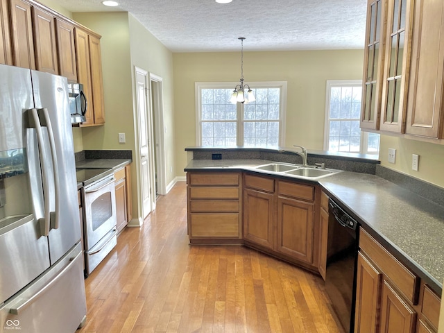 kitchen with brown cabinets, dark countertops, appliances with stainless steel finishes, a sink, and a peninsula