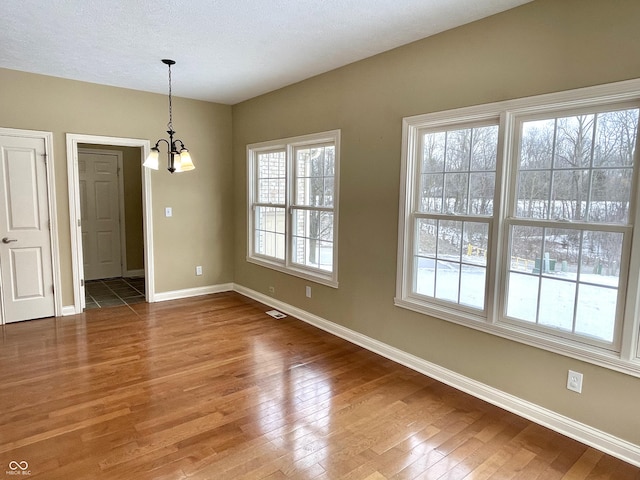 unfurnished dining area featuring wood-type flooring, visible vents, baseboards, and an inviting chandelier