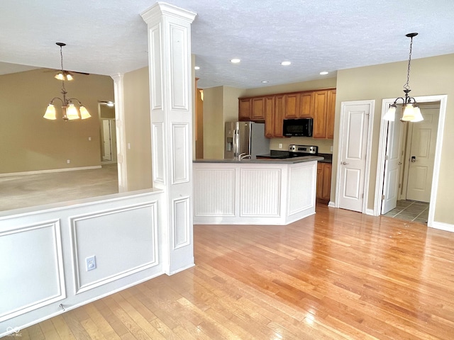 kitchen featuring decorative columns, dark countertops, light wood-style flooring, stainless steel appliances, and a notable chandelier