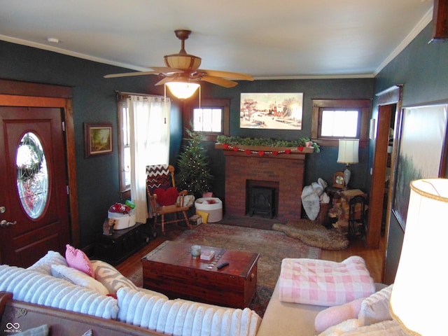 living area featuring a brick fireplace, ceiling fan, ornamental molding, and wood finished floors