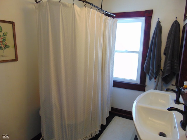 bathroom with baseboards, a shower with shower curtain, a sink, and a healthy amount of sunlight