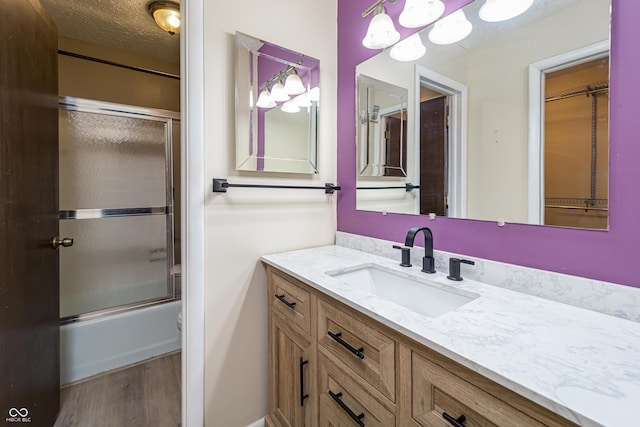 bathroom featuring vanity, wood finished floors, shower / bath combination with glass door, and a textured ceiling