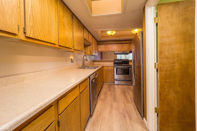 kitchen with a sink, under cabinet range hood, light wood-style floors, appliances with stainless steel finishes, and light countertops