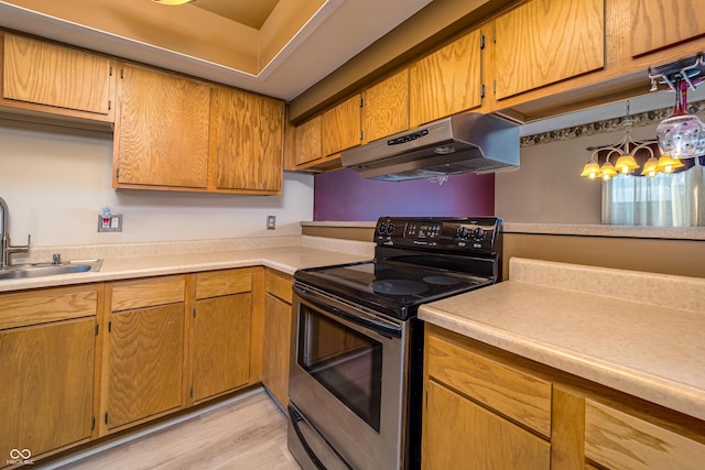 kitchen with light wood finished floors, a sink, stainless steel range with electric cooktop, light countertops, and under cabinet range hood