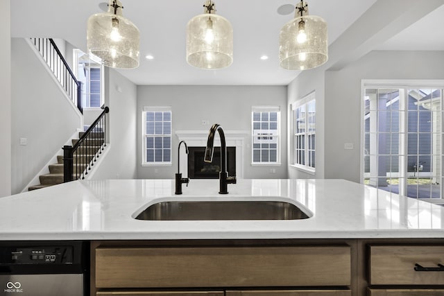 kitchen featuring stainless steel dishwasher, pendant lighting, light stone counters, and a sink