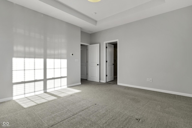 unfurnished bedroom with carpet flooring, baseboards, and a tray ceiling