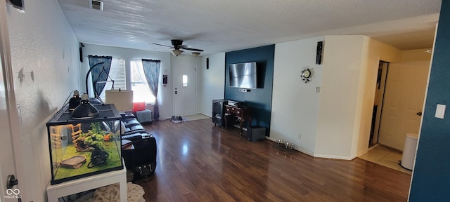 living room featuring ceiling fan, a textured ceiling, visible vents, baseboards, and dark wood-style floors