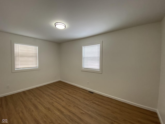 unfurnished room with visible vents, baseboards, and dark wood-style flooring