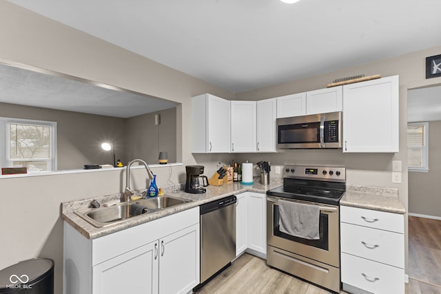 kitchen with a peninsula, white cabinetry, appliances with stainless steel finishes, and a sink