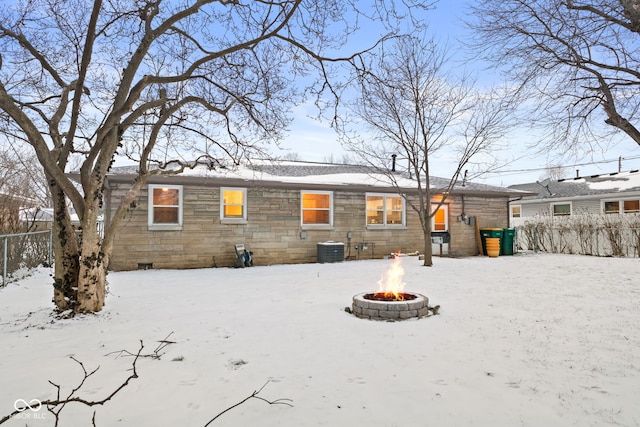 snow covered rear of property featuring central air condition unit, stone siding, fence, and a fire pit