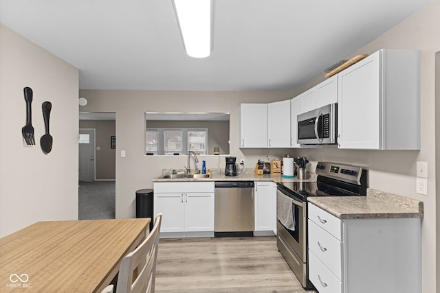 kitchen featuring light wood finished floors, light countertops, appliances with stainless steel finishes, white cabinetry, and a sink