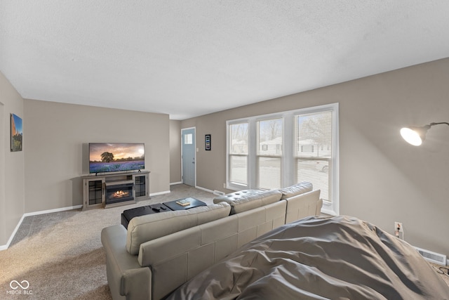 living room with a textured ceiling, light colored carpet, visible vents, baseboards, and a glass covered fireplace