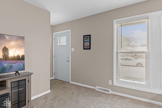 foyer entrance with a wealth of natural light, visible vents, light carpet, and baseboards