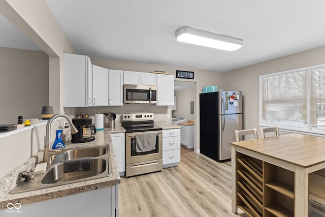 kitchen featuring white cabinets, light wood-style flooring, stainless steel appliances, light countertops, and a sink