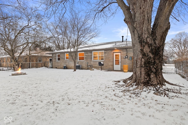 snow covered house with central air condition unit, an outdoor fire pit, and fence