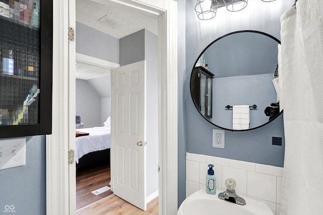 bathroom with visible vents, vaulted ceiling, a sink, a textured ceiling, and wood finished floors