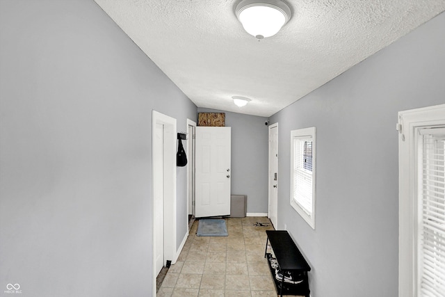 doorway with a textured ceiling, light tile patterned floors, and baseboards