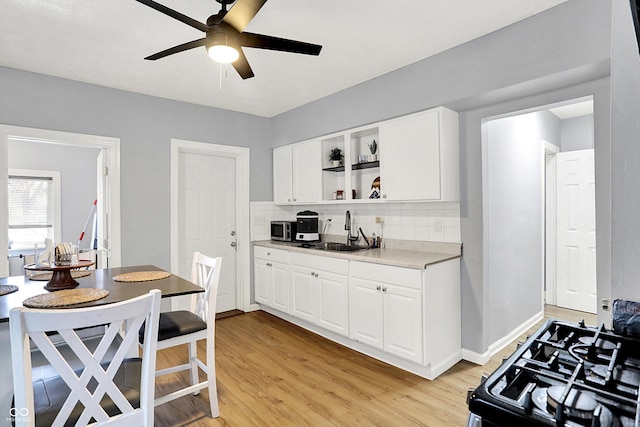 kitchen with a sink, black gas stove, light wood-style floors, open shelves, and backsplash