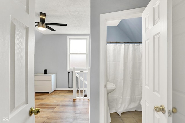 full bath featuring ceiling fan, wood finished floors, curtained shower, vaulted ceiling, and a textured ceiling