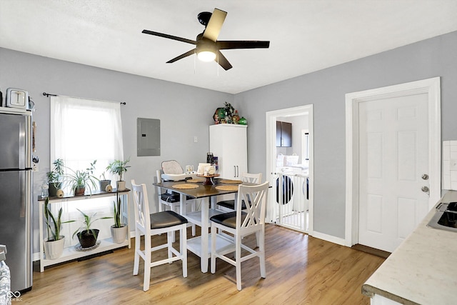 dining space featuring light wood-style flooring, electric panel, baseboards, and a ceiling fan