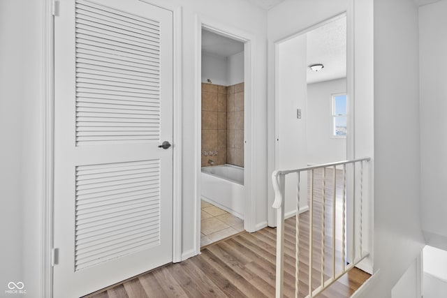 hallway with light wood finished floors, baseboards, and an upstairs landing