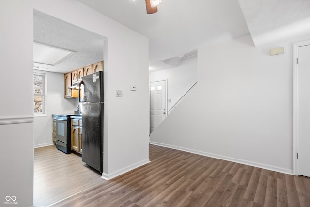 kitchen with under cabinet range hood, electric range, baseboards, light wood-style floors, and freestanding refrigerator