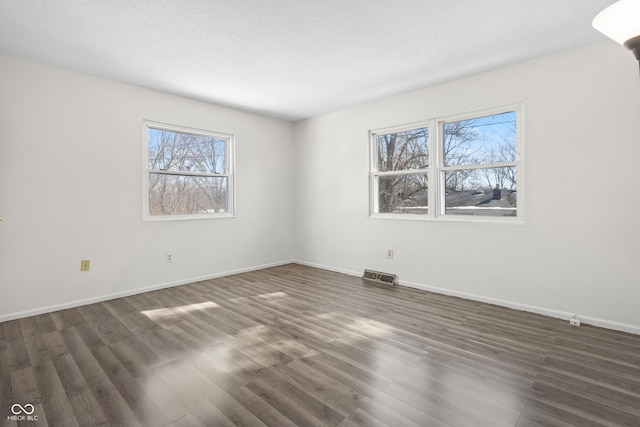 spare room with baseboards, visible vents, and dark wood-style flooring