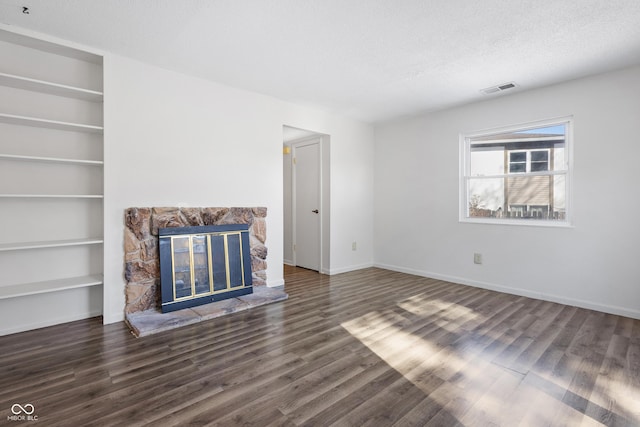 unfurnished living room with visible vents, dark wood finished floors, a textured ceiling, and a stone fireplace