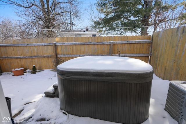 yard layered in snow with fence, a hot tub, and central AC unit