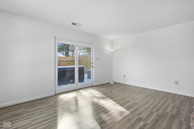 spare room featuring a textured ceiling, wood finished floors, visible vents, and baseboards