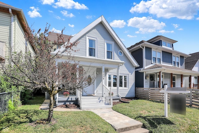 view of front facade with covered porch, a front yard, and fence