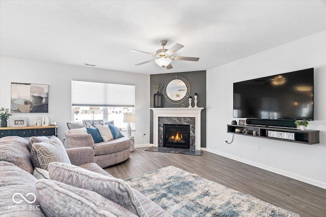 living area featuring dark wood-type flooring, a high end fireplace, visible vents, and baseboards