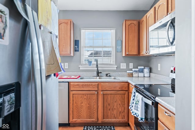 kitchen with appliances with stainless steel finishes, a wealth of natural light, light countertops, and a sink