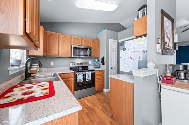 kitchen featuring light countertops, appliances with stainless steel finishes, light wood-style floors, vaulted ceiling, and a sink