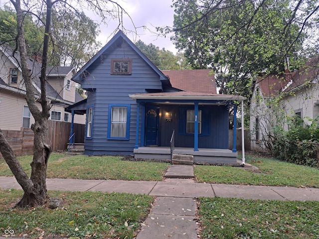 view of front facade with covered porch, a shingled roof, fence, a front lawn, and board and batten siding