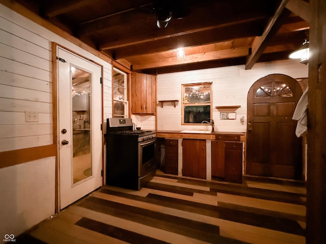 kitchen featuring beam ceiling, wood walls, a sink, wood finished floors, and stainless steel gas range oven