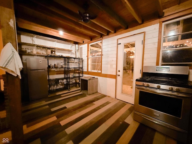 interior space with ceiling fan, wooden walls, stainless steel range with gas cooktop, freestanding refrigerator, and beamed ceiling