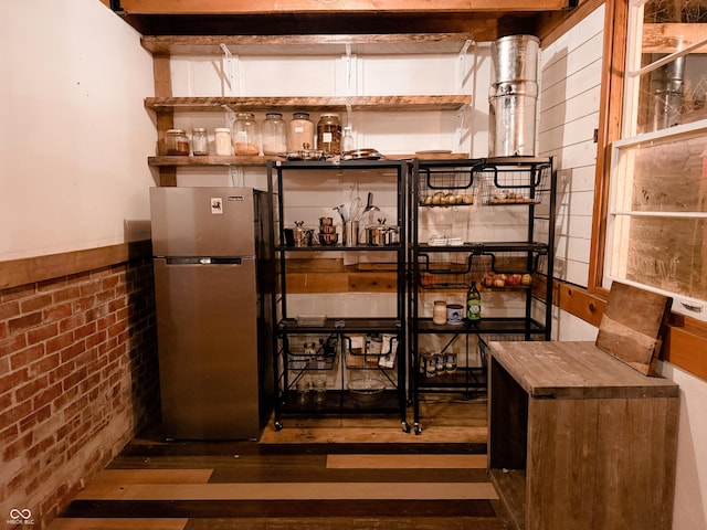 bar featuring freestanding refrigerator and brick wall