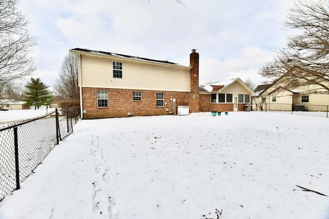 snow covered rear of property with brick siding, a chimney, and fence