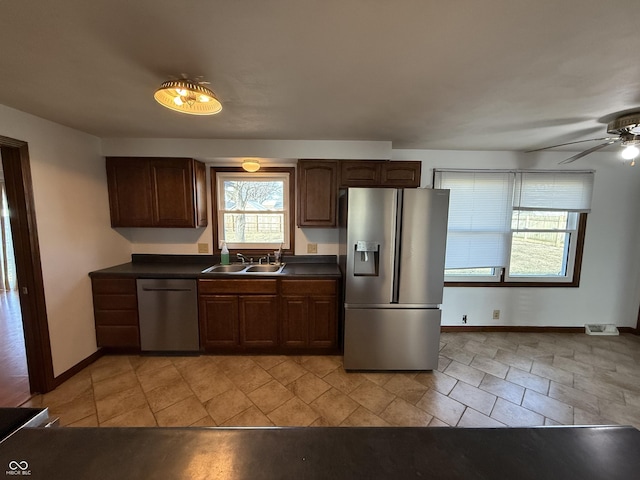 kitchen with stainless steel appliances, dark countertops, a sink, and dark brown cabinetry