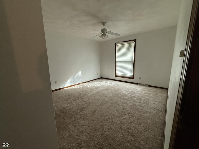 carpeted spare room featuring a ceiling fan, visible vents, and baseboards